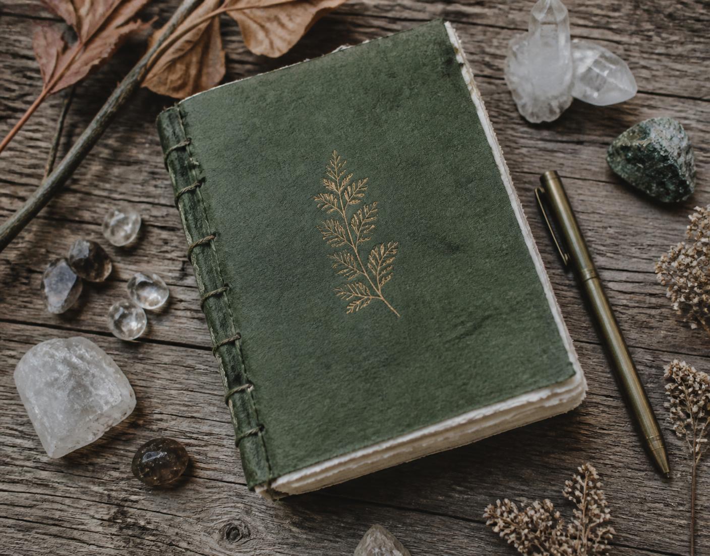 Caderno artesanal sobre madeira com cristais, folhas e caneta